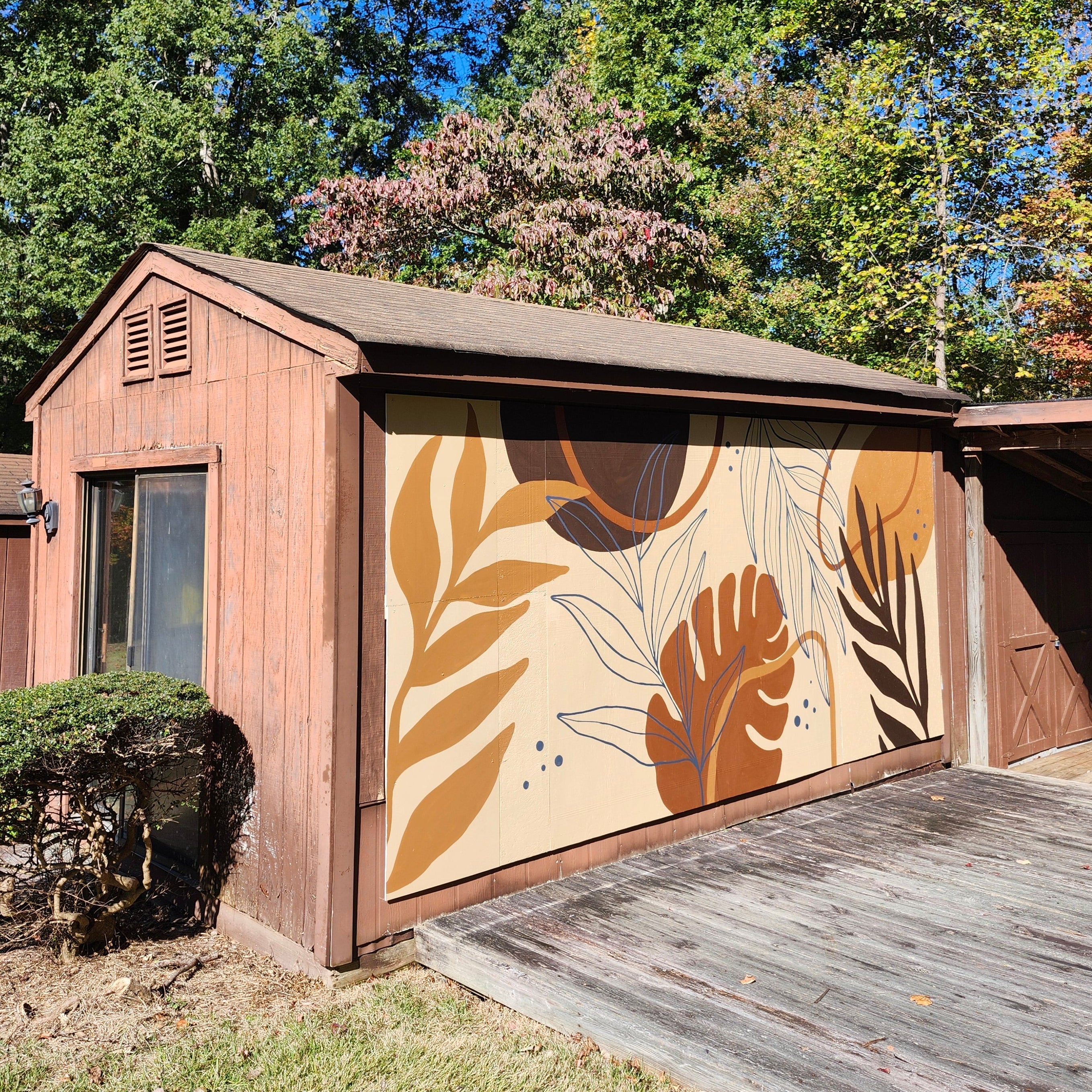 Wooden shed with a decorative mural on the outside of it. featuring leaf and abstract patterns.