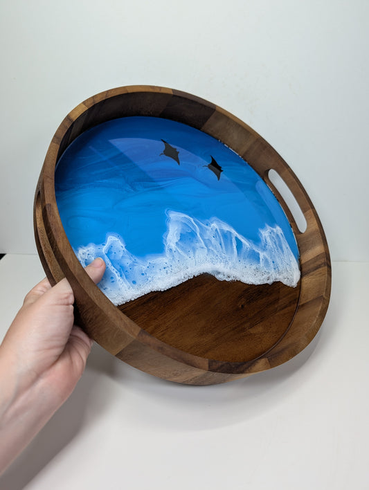 Wooden serving tray with a blue and white resin design held by a hand on a white background