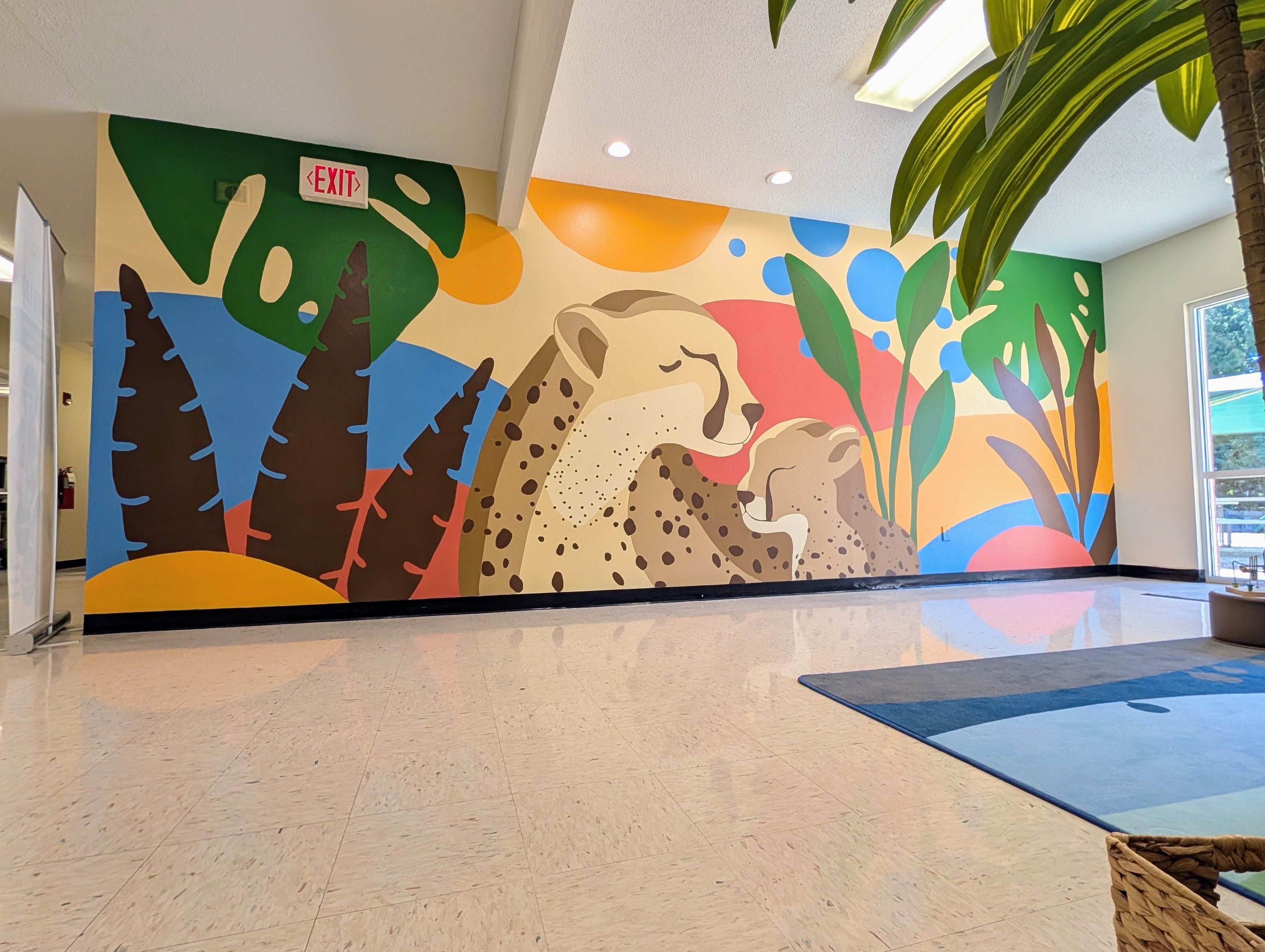 Colorful mural of a cheetah and its cub on a wall in a building lobby.